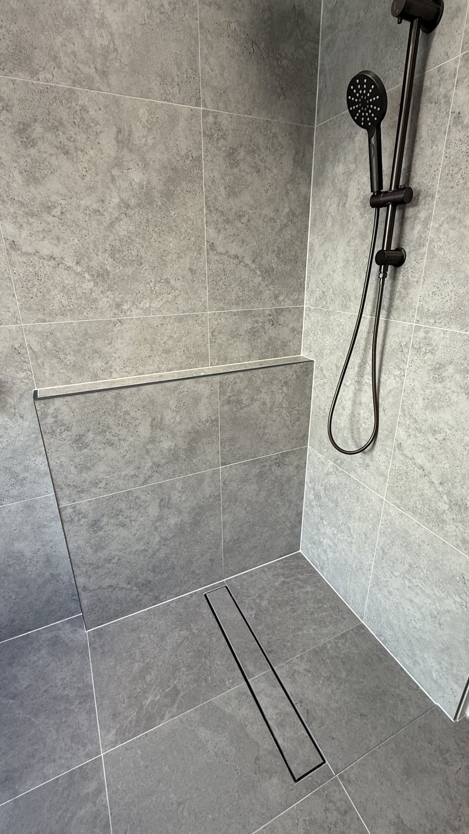 Grey tiled shower with clean silicone joints and black shower fittings